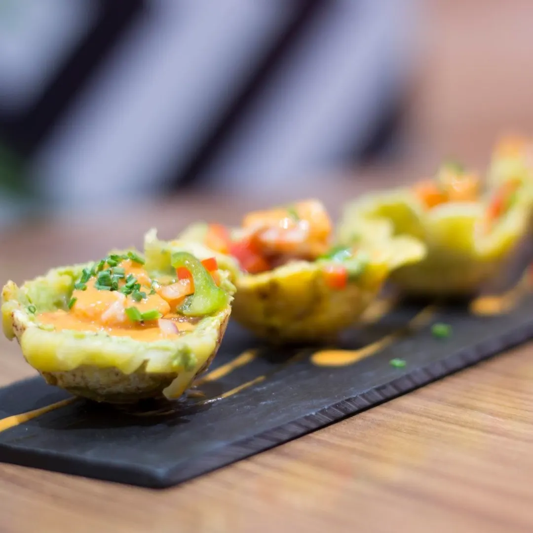 Cuatro mitades de aguacate rellenas con salsa y pimiento verde, en fila sobre una pizarra