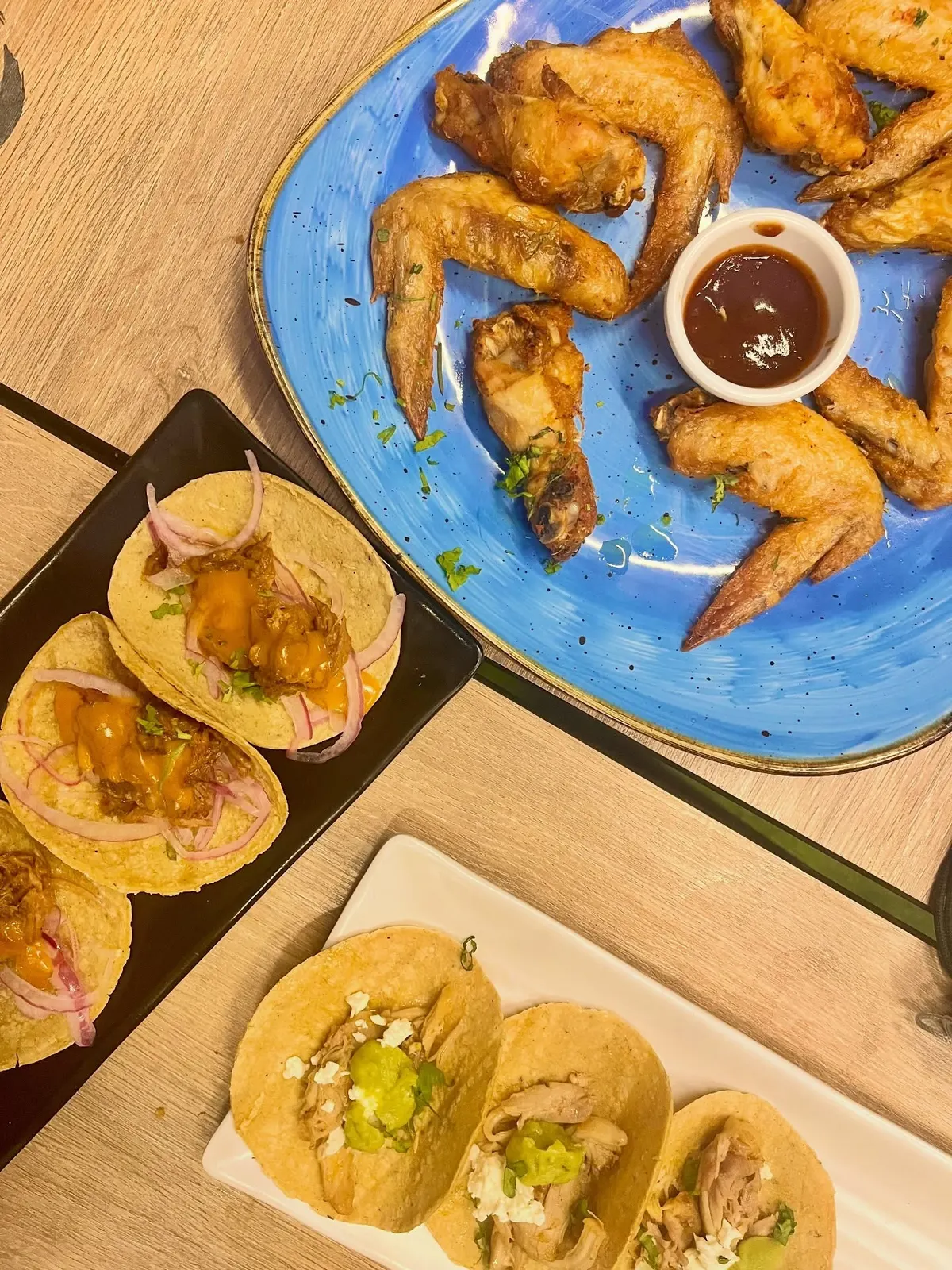 Plato de alitas con salsa y dos tablas de tacos de maíz, vistos desde arriba
