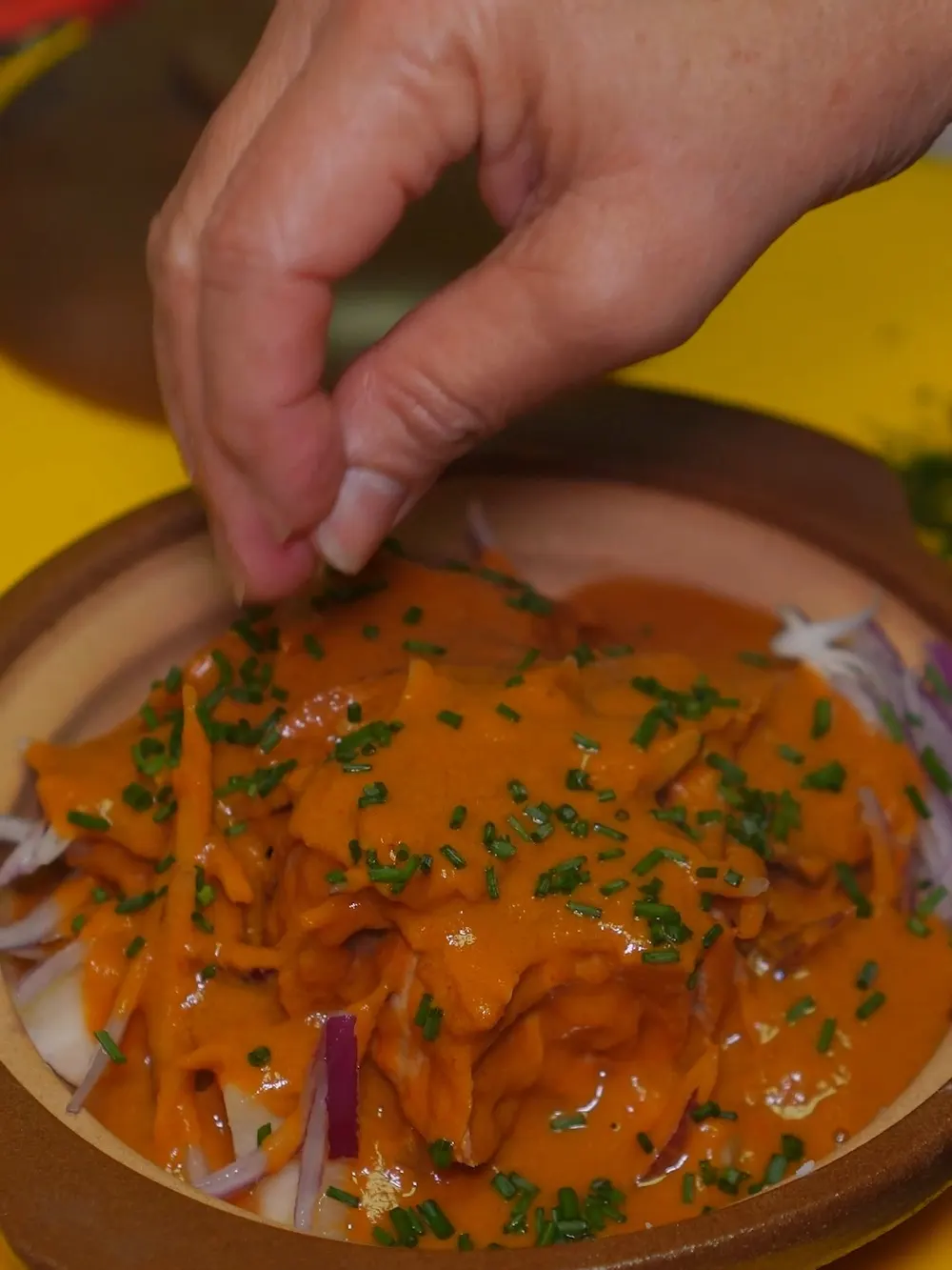 Una mano espolvorea cebollino sobre una cazuela de barro con carne en salsa