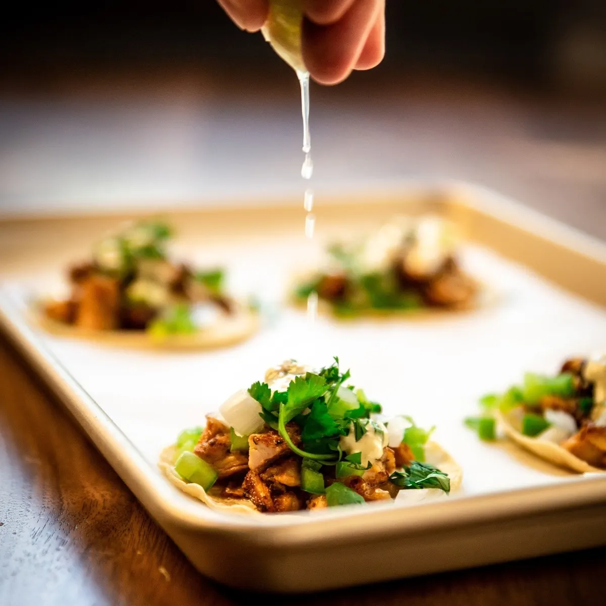 Una mano exprime lima sobre una bandeja de tacos con cilantro y cebolla