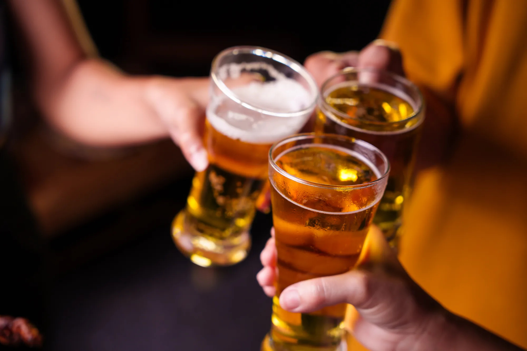Varias manos brindan con vasos de cerveza en un local con poca luz