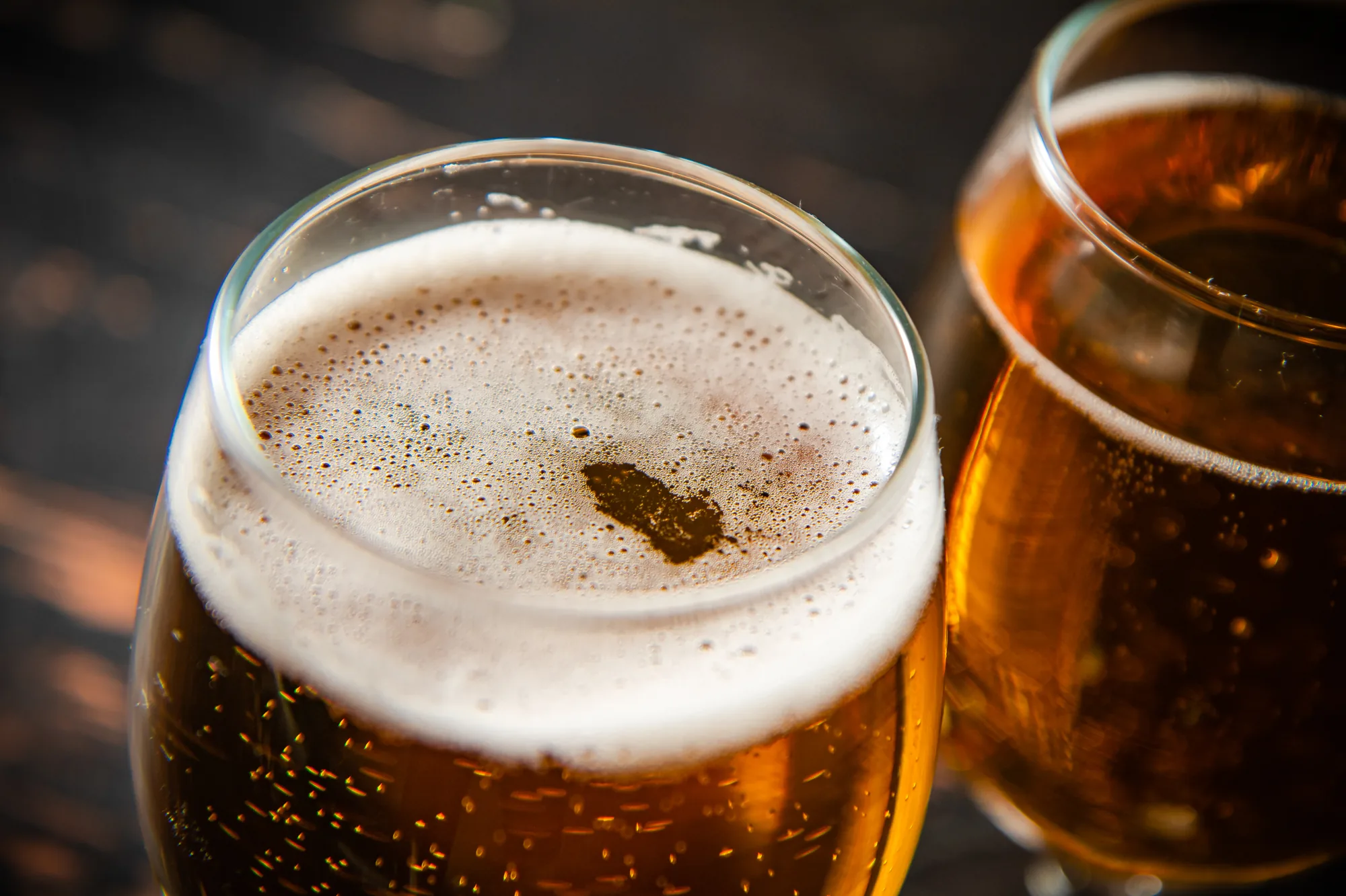 Dos vasos de cerveza dorada con espuma, en primer plano y con luz cálida