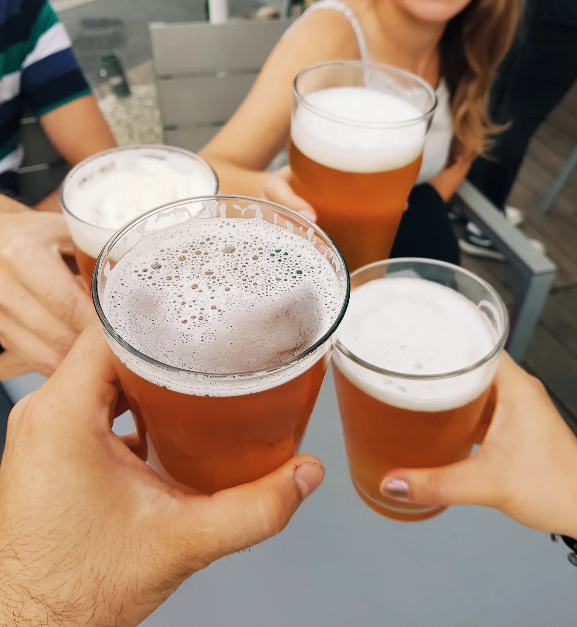 Dos manos brindan con vasos de cerveza con mucha espuma, a la luz del día